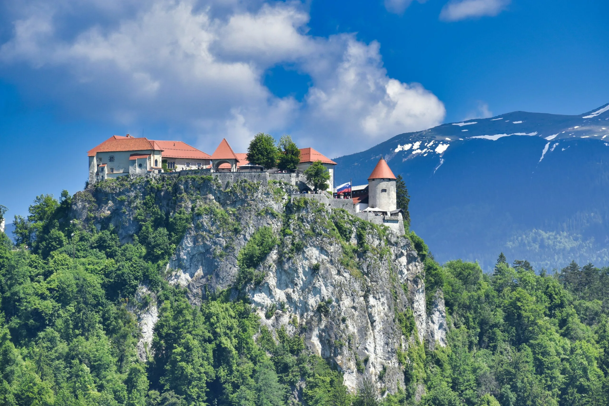 Bled Castle perched on a cliff overlooking Lake Bled with snow-capped mountains in the background.