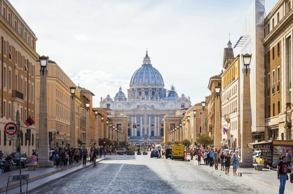 A street view leading towards St. Peter's Basilica, with its dome prominently visible.