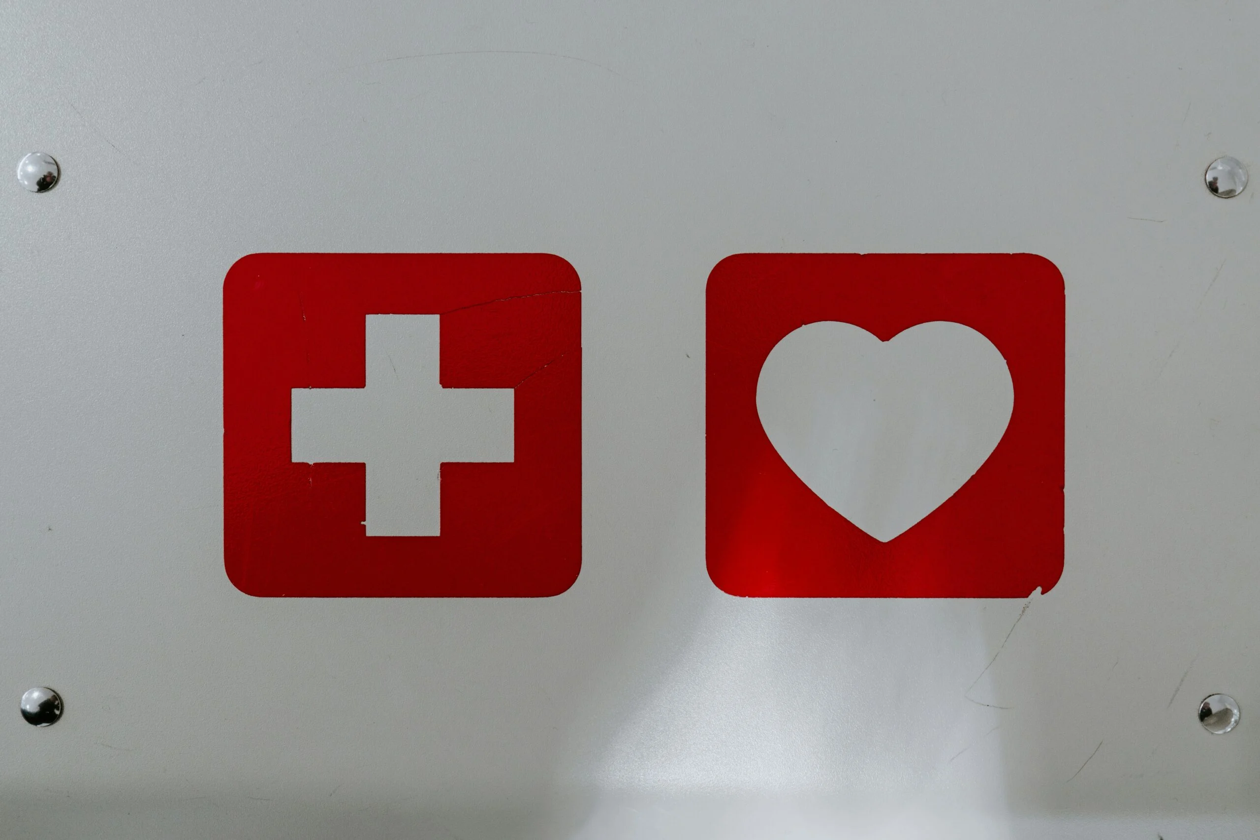 A close-up of a white surface featuring two red square icons: one with a white cross (medical symbol) and the other with a white heart.
