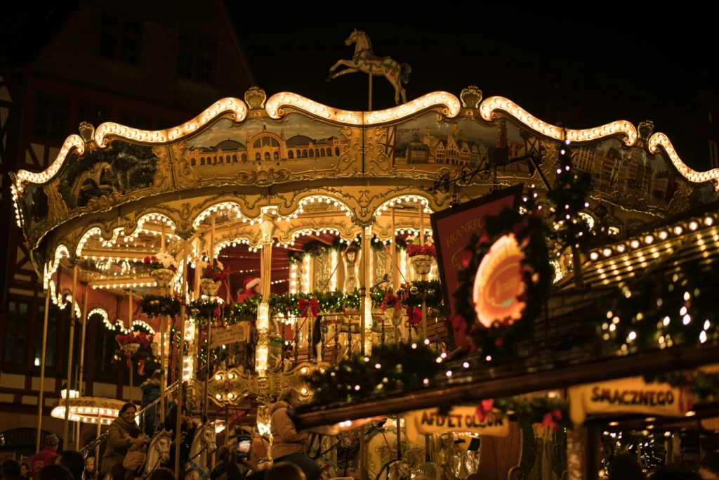 A brightly lit carousel with horses and ornate decorations, spinning at night, part of a Christmas market.