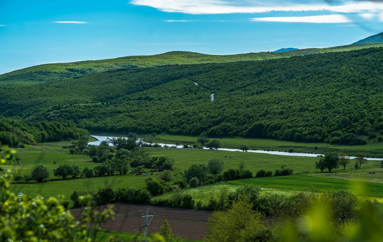 A scenic view of a river valley with green hills and a bright blue sky.