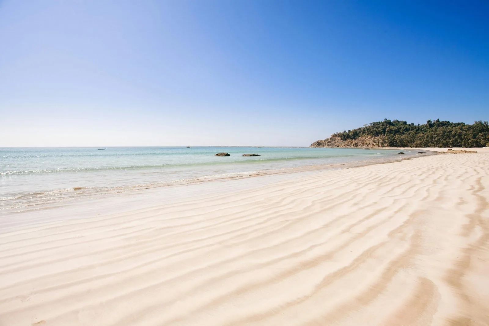 A beautiful, wide, white-sand beach with a calm blue ocean and clear sky.