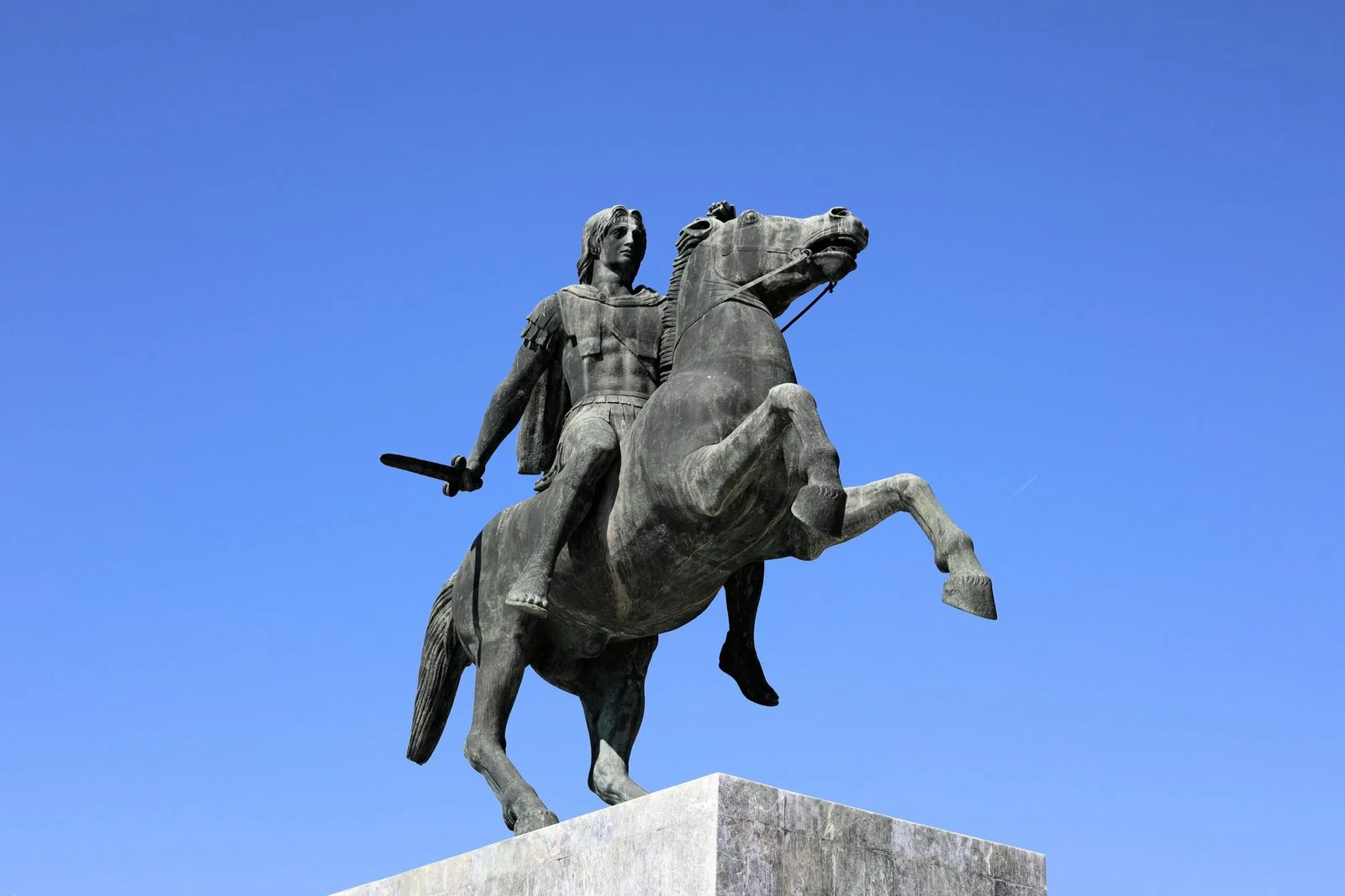 A large bronze equestrian statue of a historical figure, rearing on its hind legs against a clear blue sky.