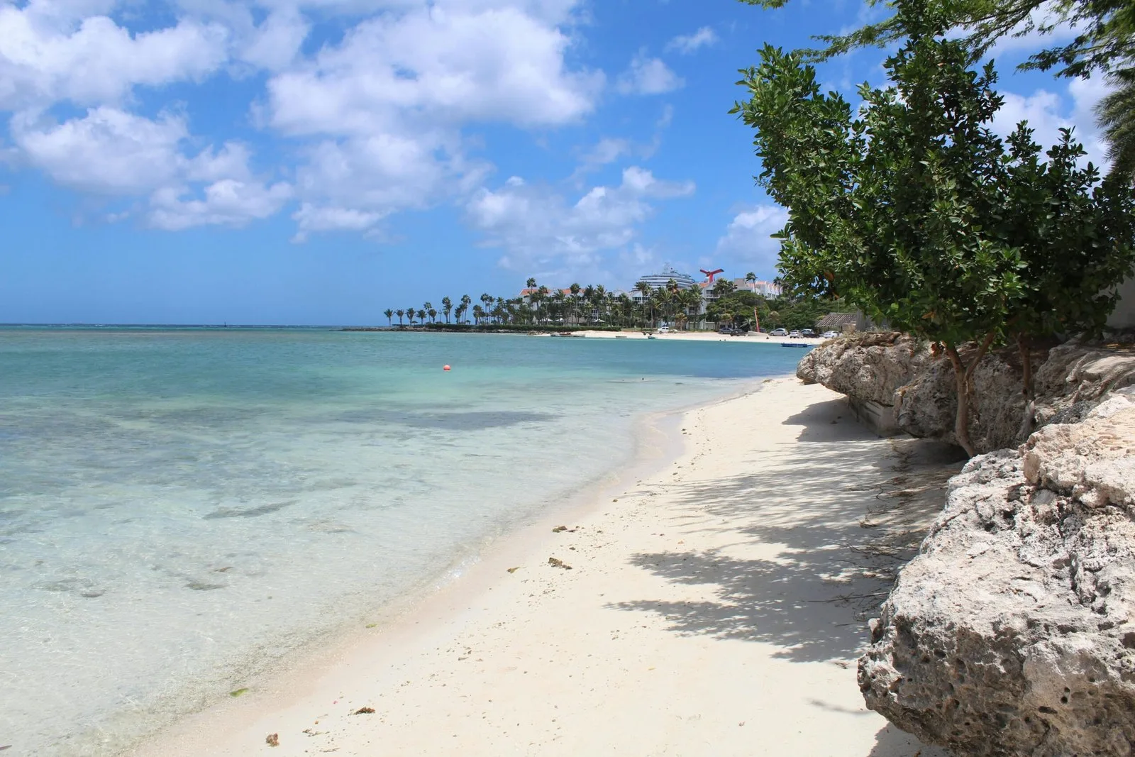 A pristine tropical beach with white sand, turquoise water, and lush green vegetation.