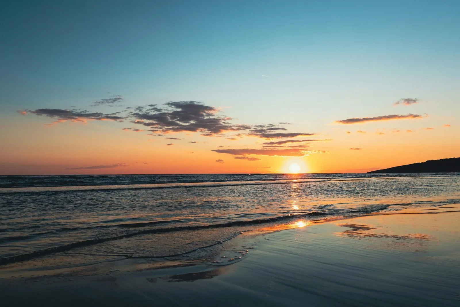 A beautiful sunset over the ocean, with the sun setting on the horizon and reflecting on the water.