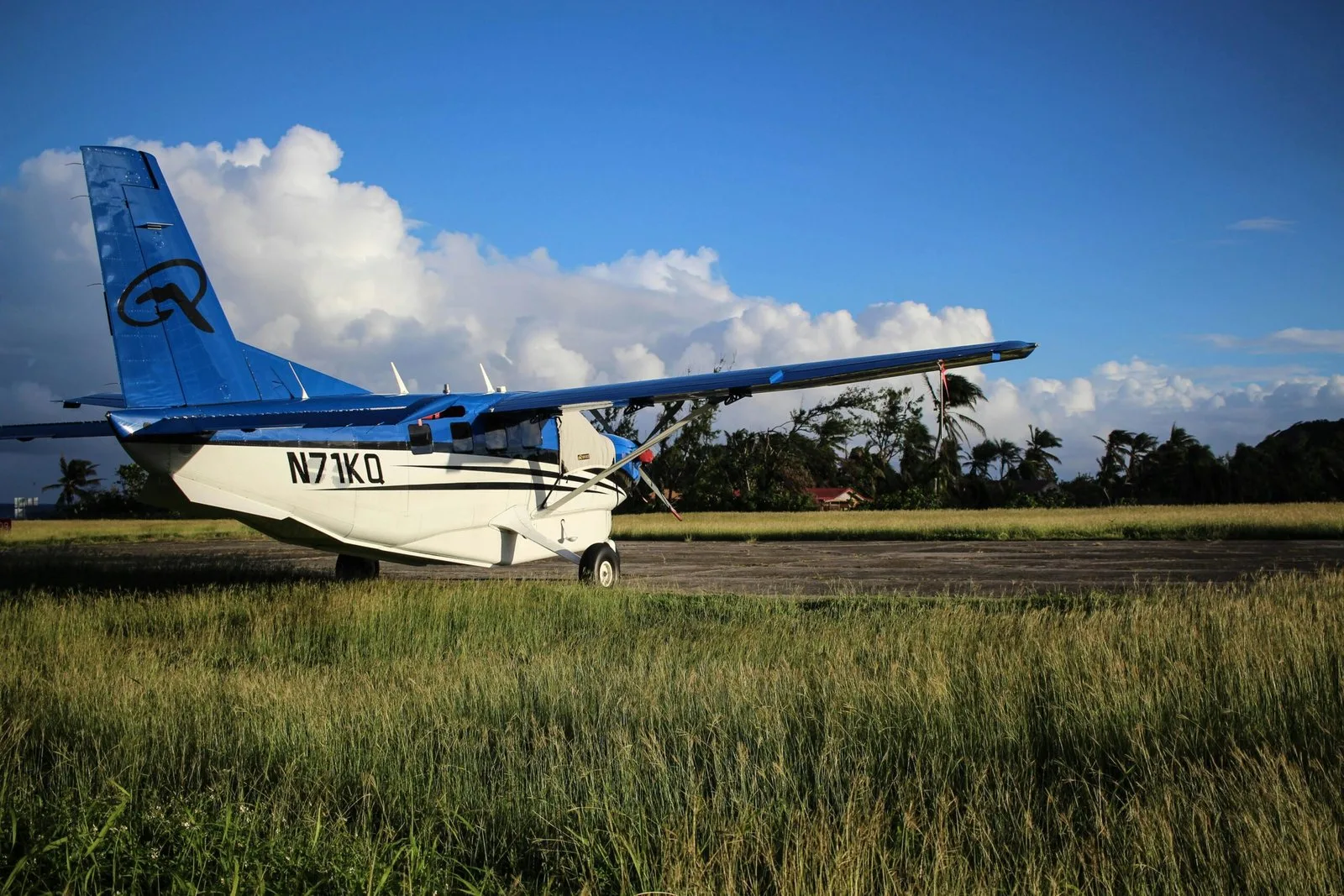 A small plane parked on a grassy airfield under a bright, cloudy sky.