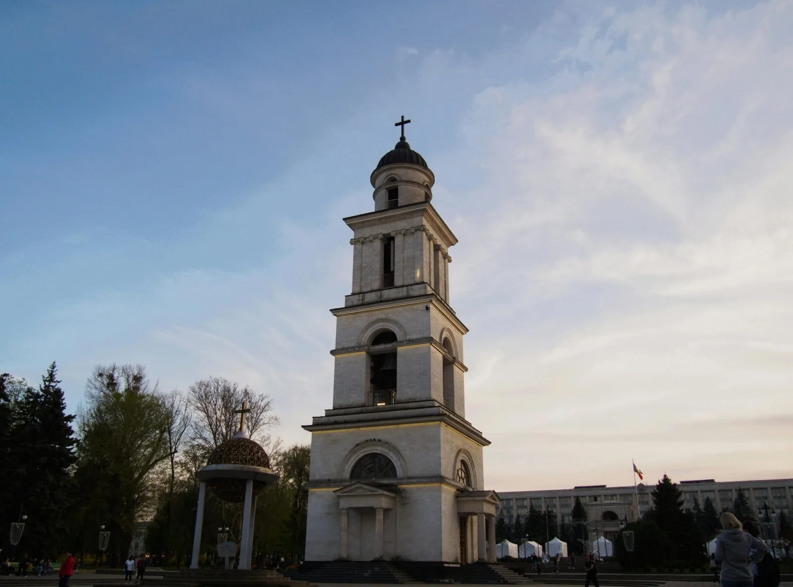 A large white bell tower and church with a golden dome against a blue and cloudy sky.
