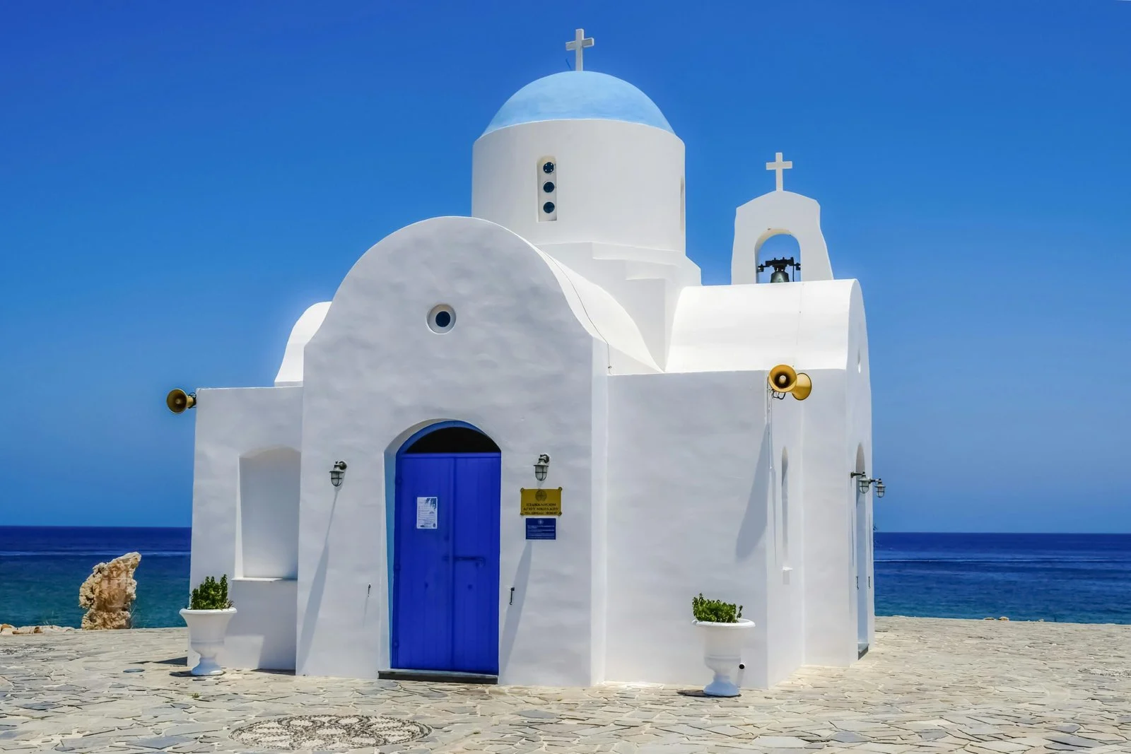 The iconic whitewashed church with a blue dome is a hallmark of Mediterranean architecture. This specific chapel is the Agios Nikolaos Chapel, situated in the Paralimni area. It's a popular spot for weddings and is located next to a small fishing harbor.
