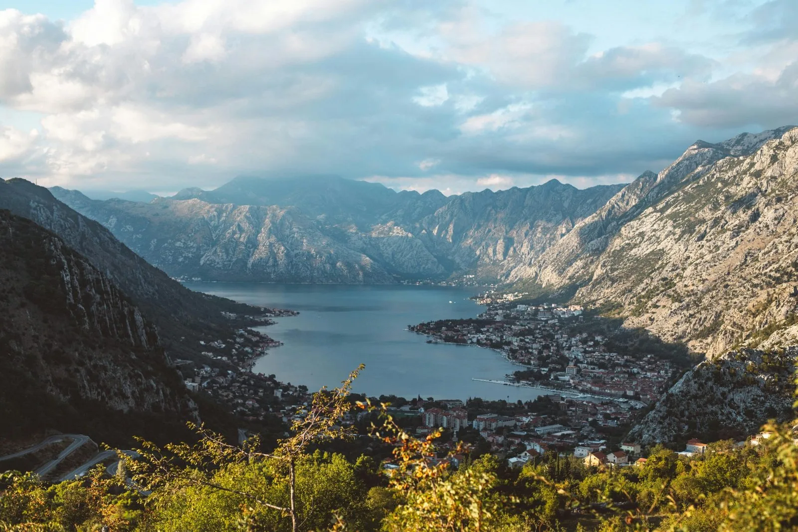 A panoramic view of a bay surrounded by dramatic, rocky mountains under a cloudy sky.