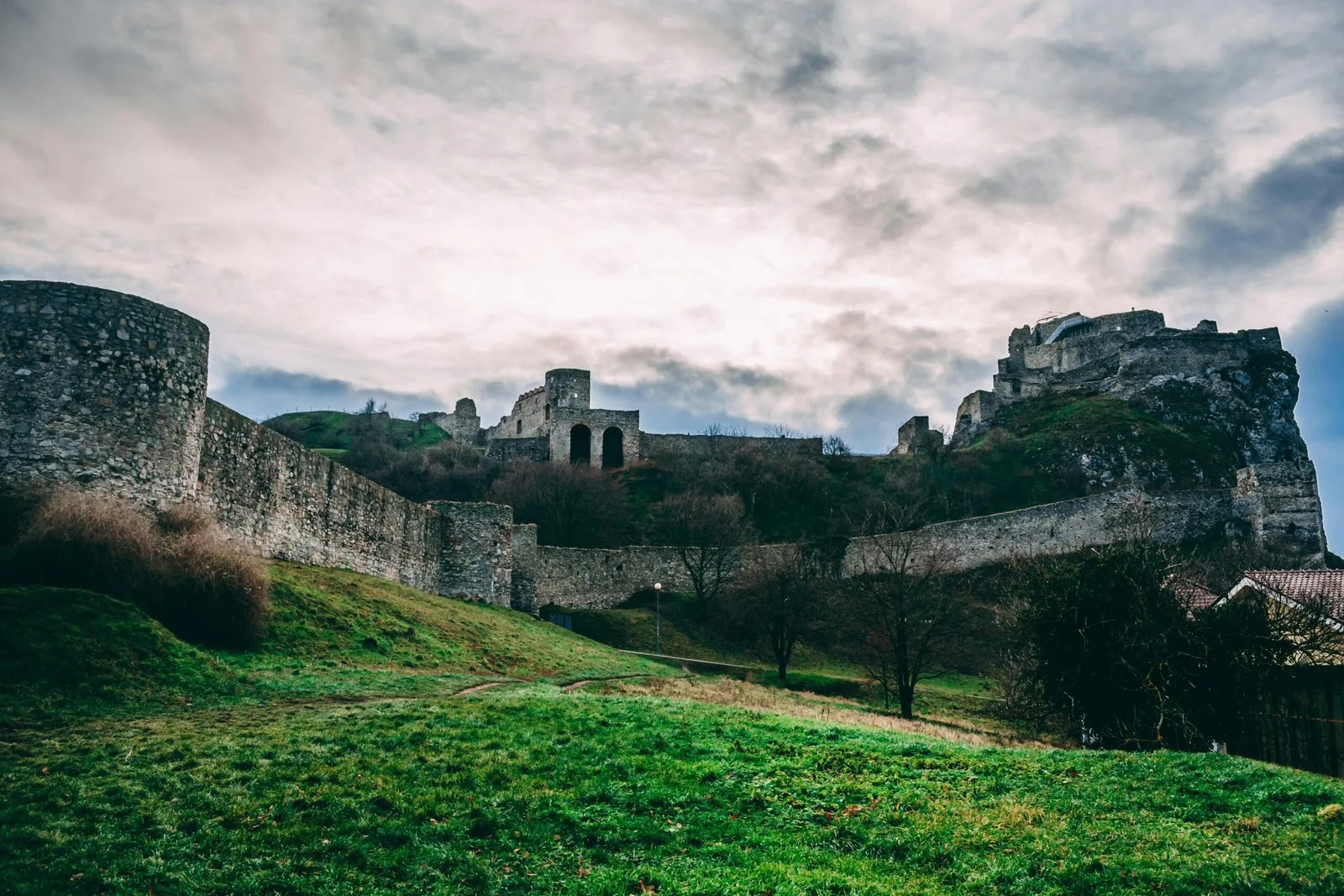 The ruins of a medieval castle on a hill surrounded by green grass and trees.