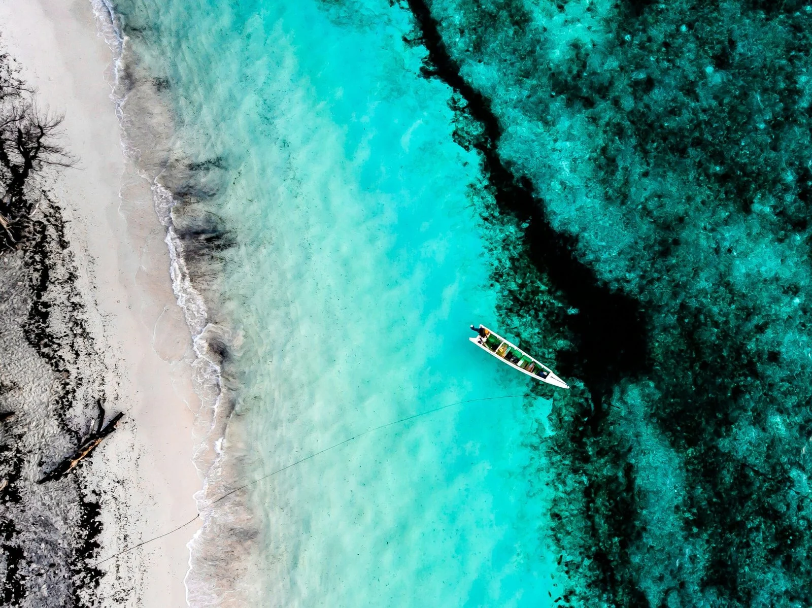 An aerial view of a white sand beach and coral reef with vibrant turquoise water.