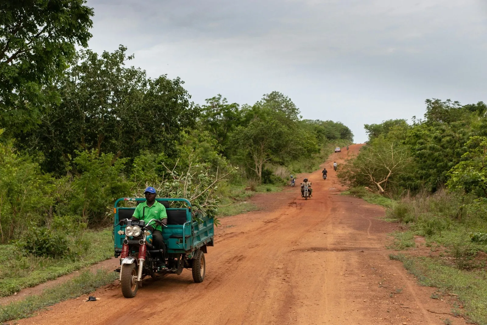 A dirt road winding through a rural, green landscape with a motorcycle and a person visible in the distance.
