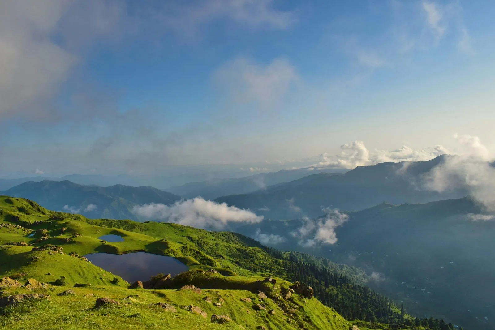 A mountain landscape with a small lake and clouds in the valleys.
