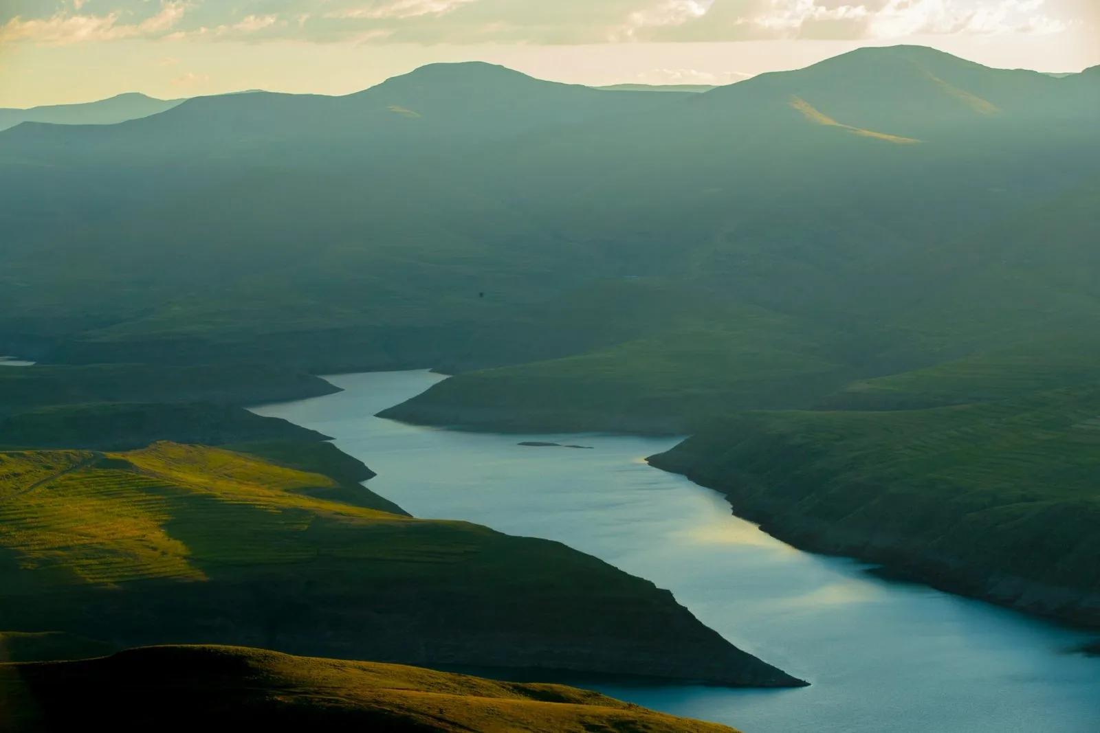 An aerial view of a winding river or reservoir flowing through a mountainous landscape.