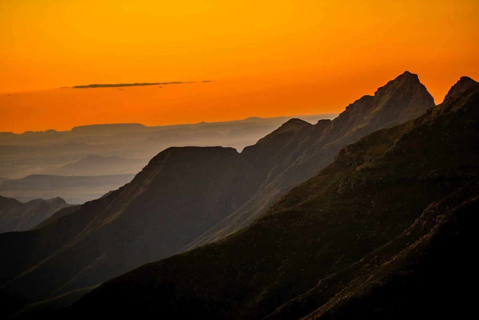 A dramatic sunset over a range of jagged mountains with a vibrant orange sky.