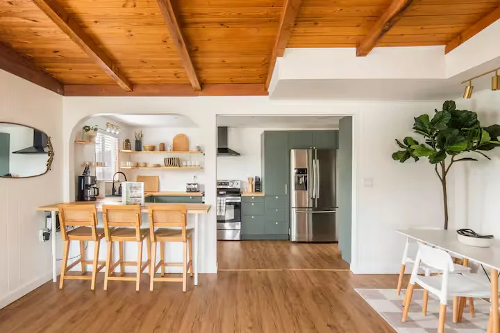 Quiet off-season vacation rental kitchen with exposed wooden beams, green cabinets, breakfast bar and bright open layout.