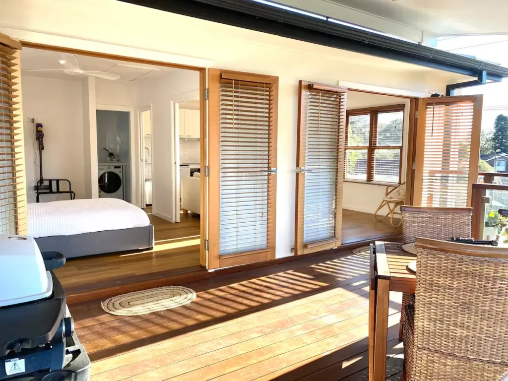 Sunlit wooden deck veranda with wicker seating and open bi-fold doors into a cozy off-season holiday suite.