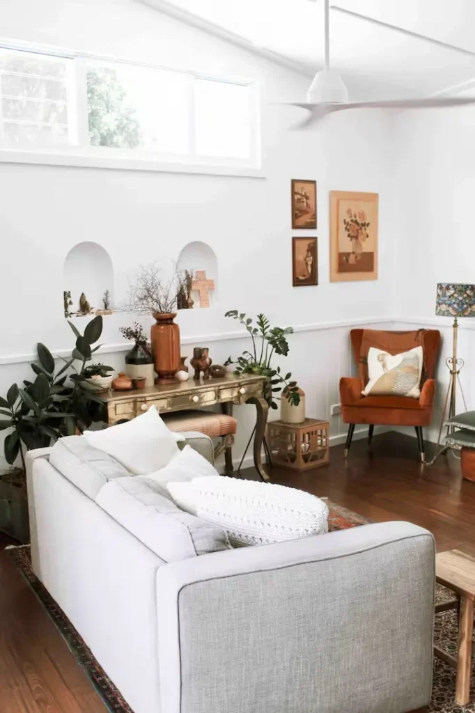Bright, airy living room in an off-season rental with white walls, modern sofa, terracotta armchair, wood floors and greenery