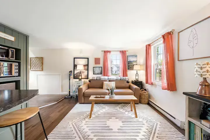 Sunlit vacation rental living room with cozy sofa, patterned rug and pastel curtains, quiet off-season atmosphere.