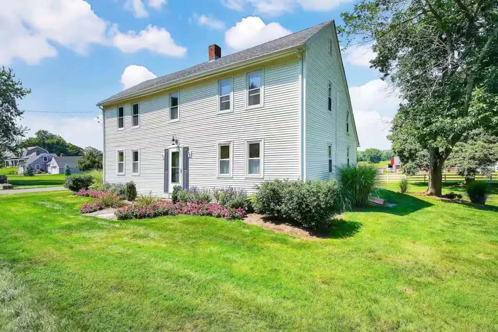 Quiet rural farmhouse with vibrant green lawn and blue sky, serene off-season charm for countryside travel and getaway.