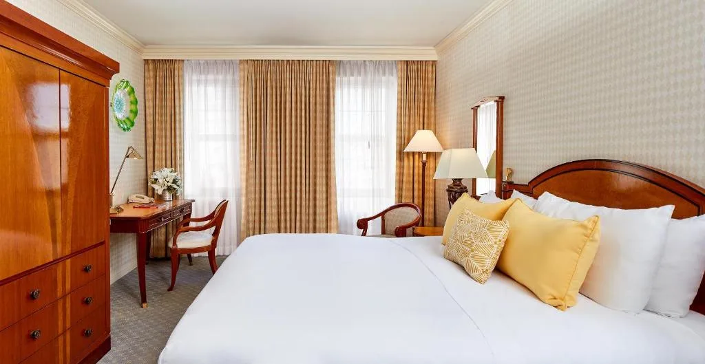 Cozy off-season travel hotel room with king bed and yellow pillows, wooden desk, lamps and soft natural light.