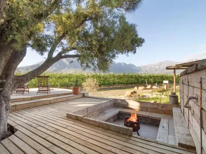 Outdoor wooden terrace overlooking empty vineyard and distant mountains, cozy fire pit glowing in off-season calm.