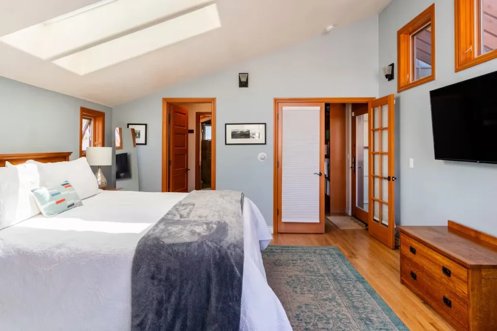 Loft bedroom in a tranquil off-season retreat with skylight, king bed, white linens and warm wooden accents.
