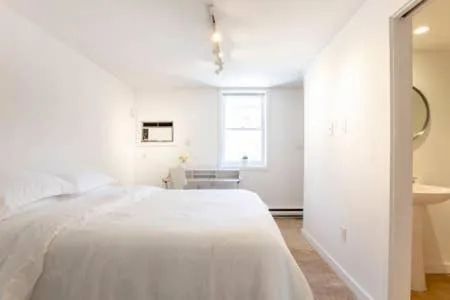 Bright minimalist guest room with crisp white linens, small desk, and en suite bath, offering a quiet off-season retreat.
