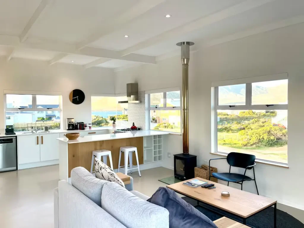 Bright coastal cottage interior with wood stove and sea views through windows, off-season calm holiday retreat.