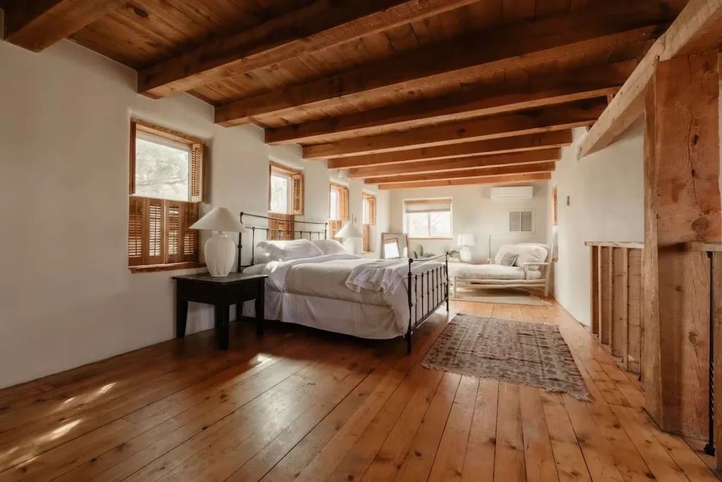 Sunlit rustic loft bedroom with exposed beams, wooden floors and cozy lounge, ideal for a peaceful off-season getaway.