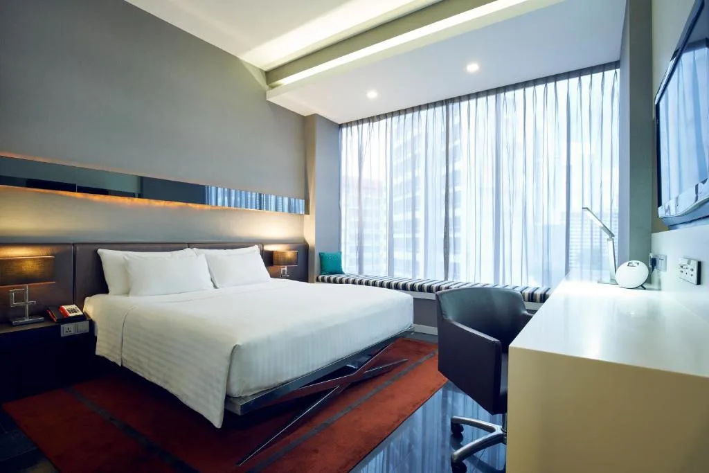 Modern hotel room with king bed and cityscape view through large windows, quiet off-season ambiance.