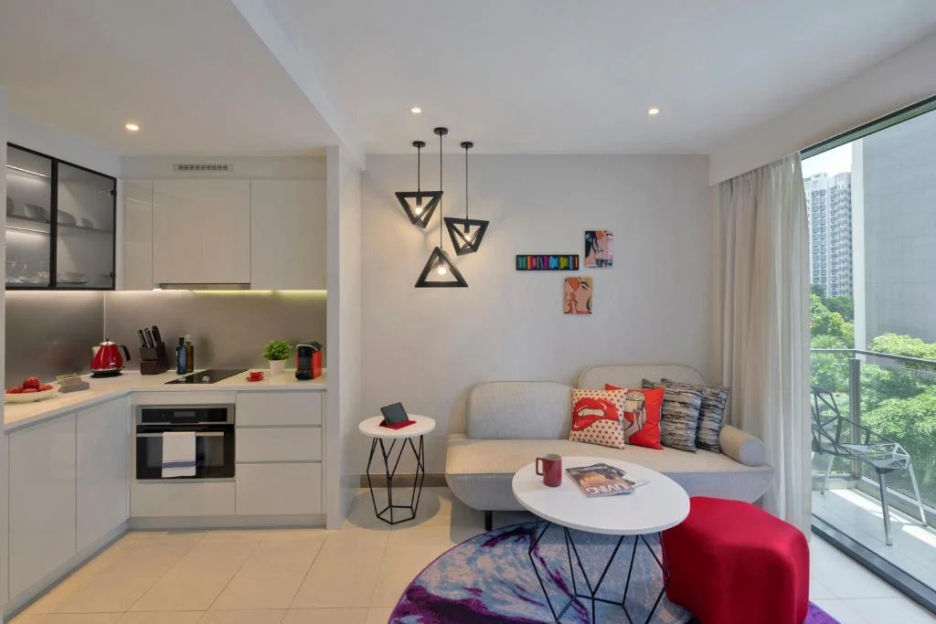 Modern vacation apartment interior with kitchenette, cozy living area and balcony overlooking greenery, off-season retreat.