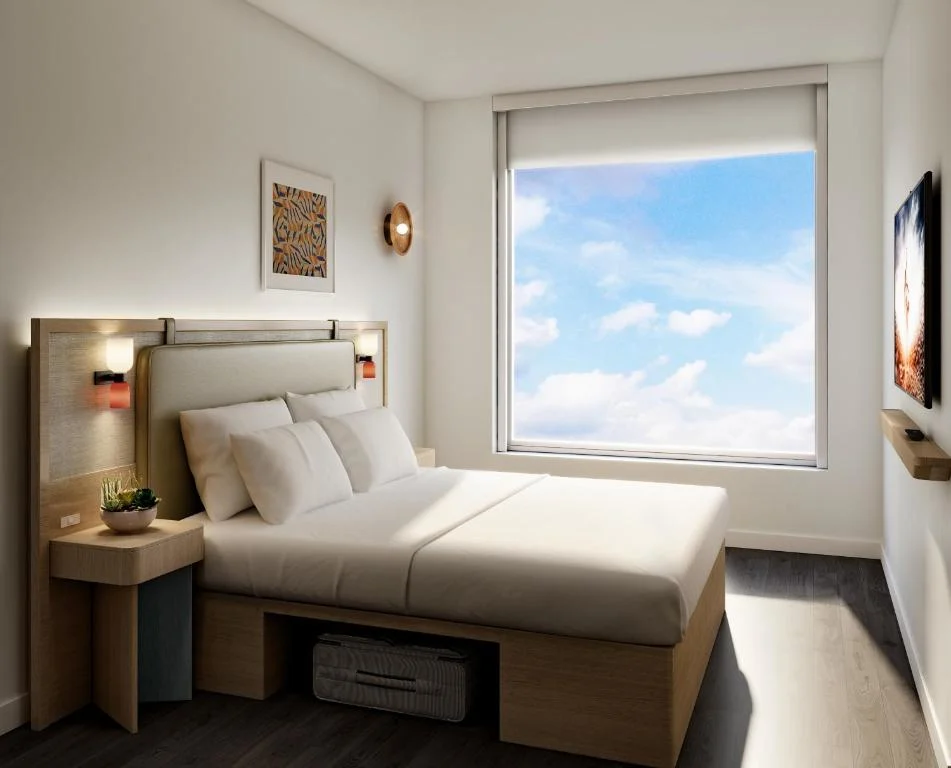 Modern hotel room with king bed and large window framing blue sky, capturing calm off-season travel vibes.
