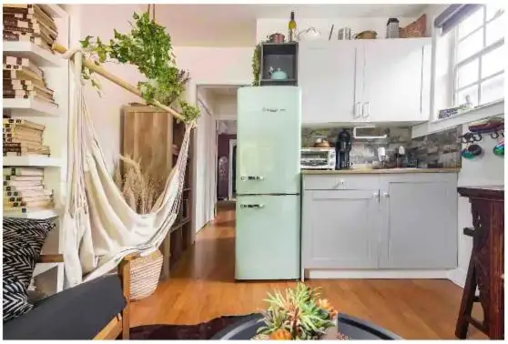 Cozy off-season vacation rental interior with hammock chair, pastel retro fridge, open kitchen and warm wood floors.