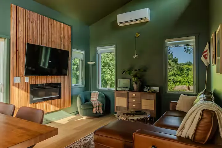 Cozy off-season cabin interior with leather sofa, green walls, wood-paneled fireplace and tranquil forest views.