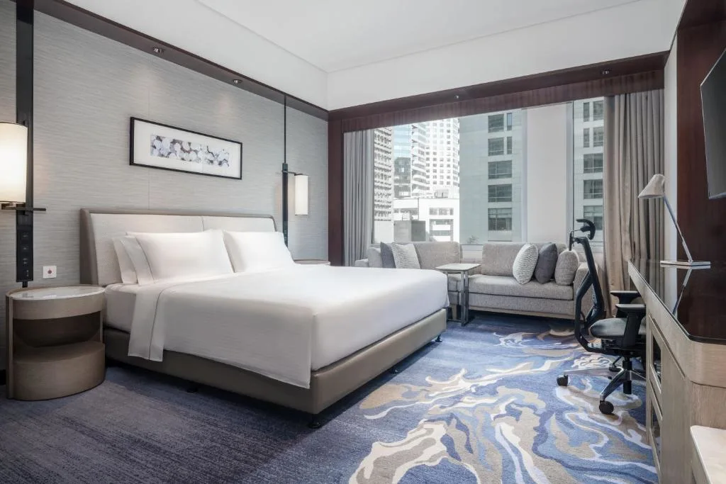Spacious modern hotel room with king-size bed, city skyline view and cozy seating, perfect quiet off-season retreat