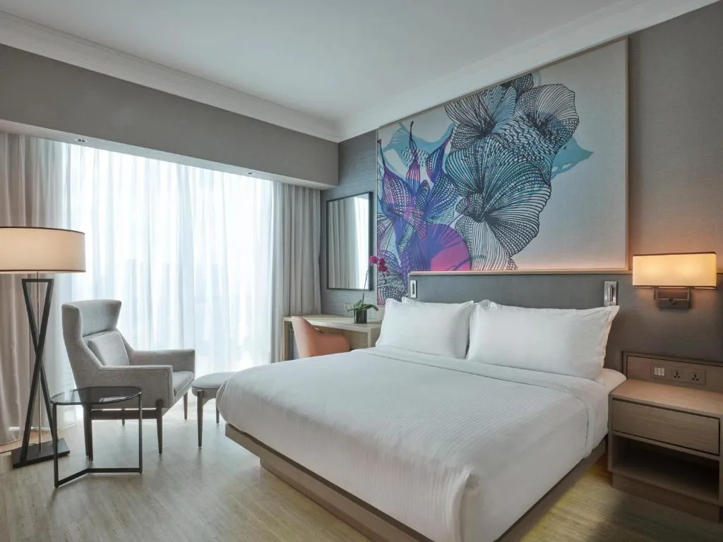 Modern hotel room with king bed and lounge chair by sheer curtains, wrapped in a peaceful off-season travel ambiance.