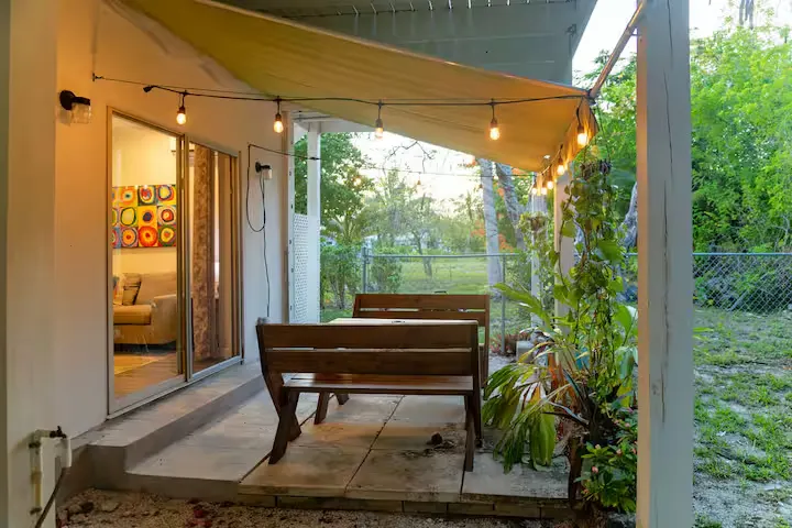 Cozy off-season getaway patio with empty wooden benches under string lights and garden view at sunset.