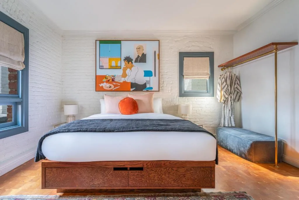 Sunlit boutique hotel bedroom with textured brick wall, vibrant artwork and serene off-season vibe for quiet getaways.