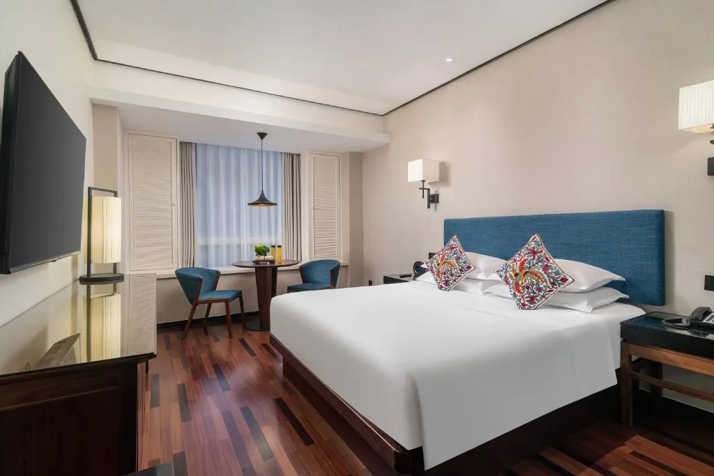 Modern hotel room with king bed, wooden floors and blue accents, window-side table and chairs in quiet off-season calm
