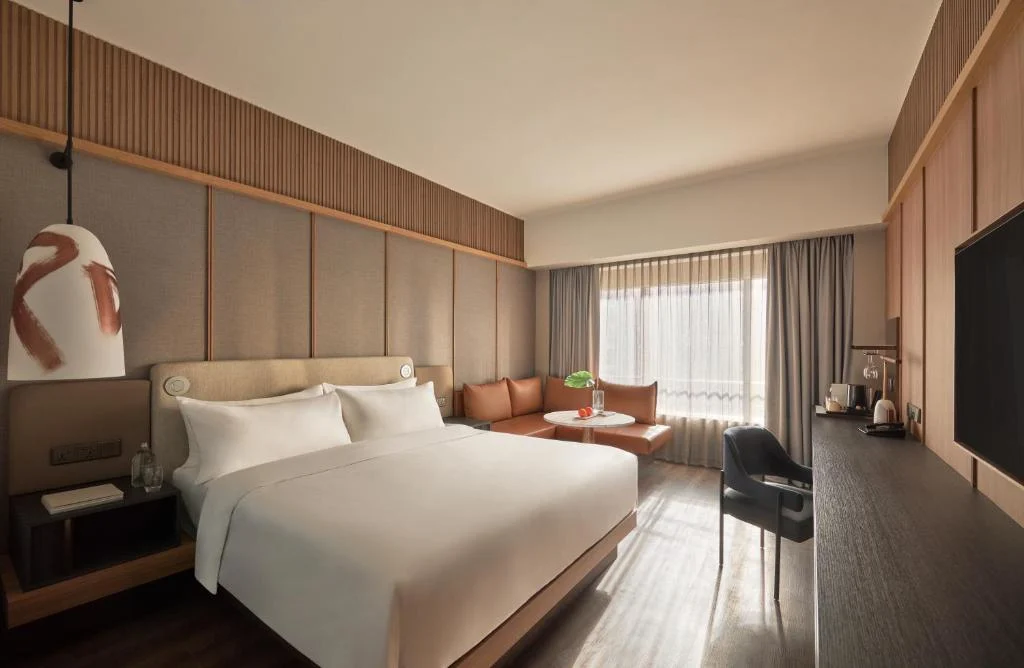Empty modern hotel room with king bed, cozy seating area and soft natural light, evoking a quiet off-season travel retreat.