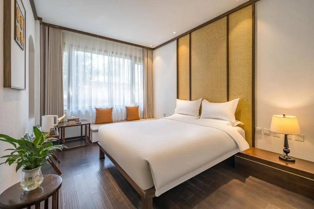 Cozy minimalist hotel bedroom with warm lighting, wood floors and bright window seat—ideal quiet off-season travel retreat.
