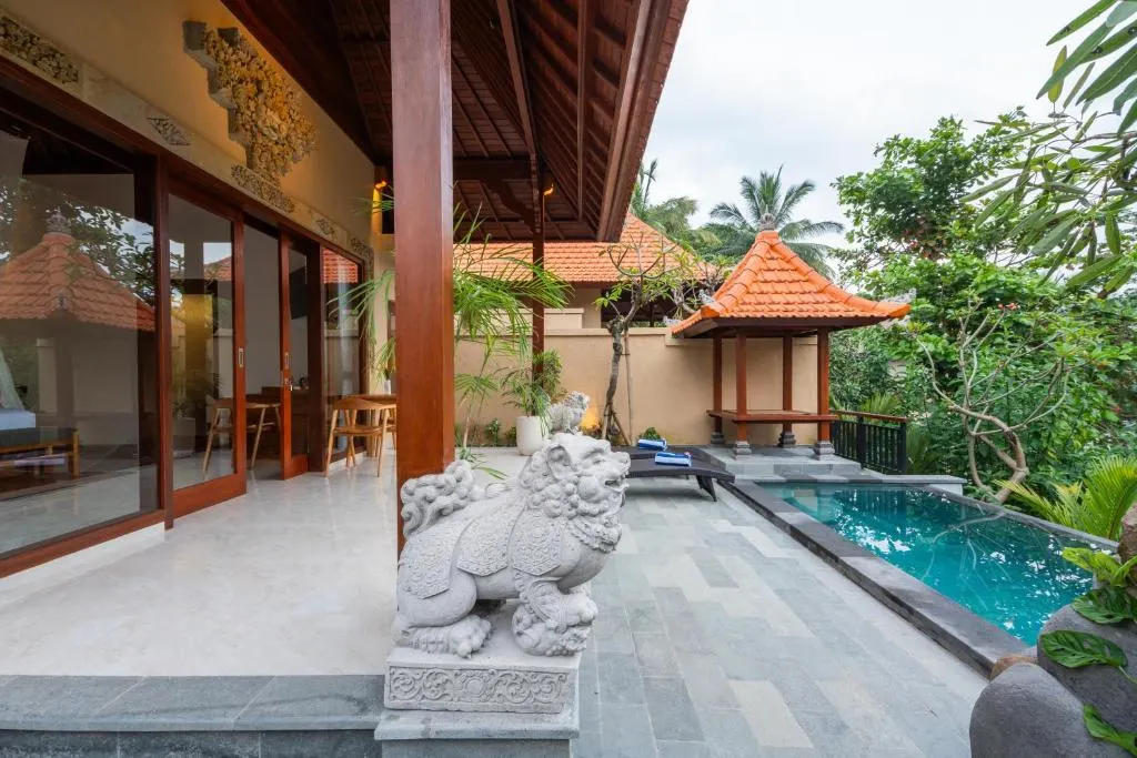 Tranquil off-season tropical resort terrace with empty pool, carved stone guardian statue, lush greenery and lounge chairs