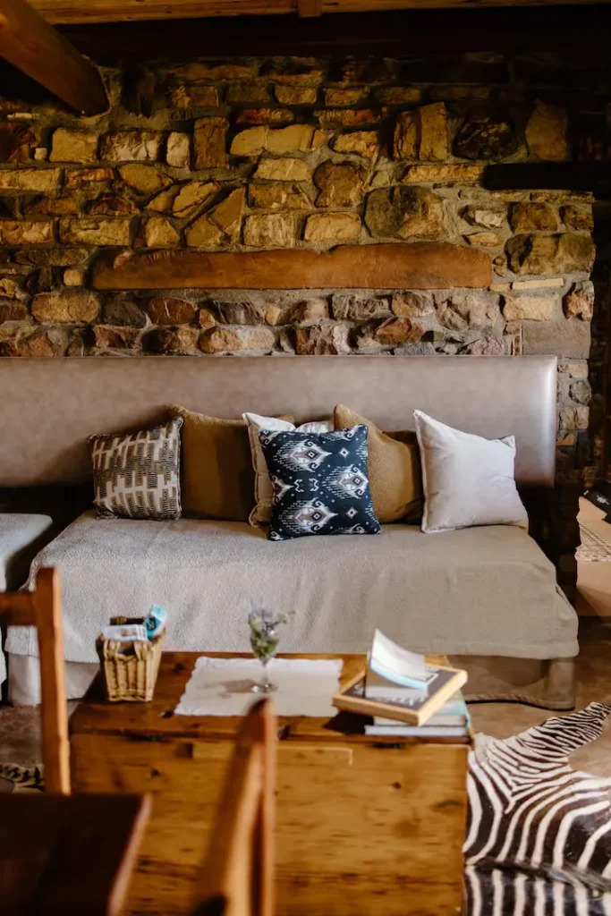 Cozy off-season rustic cabin with stone walls, patterned cushions, wooden table with books and zebra-print rug.