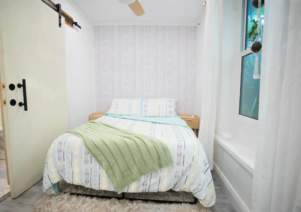 Cozy minimalist rental bedroom with pastel bedding and a seafoam green throw by a curtained window, off-season calm vibe
