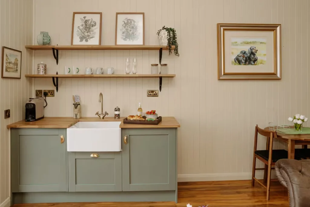 Cozy off-season travel cottage kitchenette with farmhouse sink, wooden shelves, coffee maker and empty table for getaways.