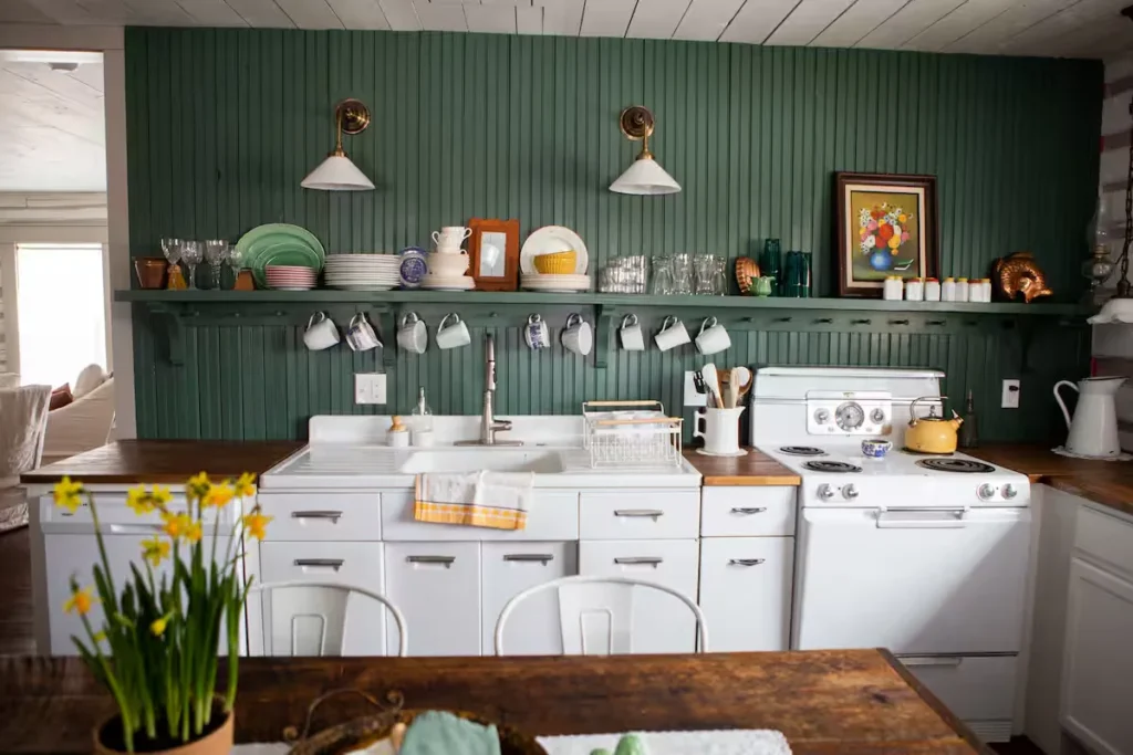 Cozy off-season getaway cottage kitchen with white cabinets, green paneled walls and daffodils on rustic wood table.