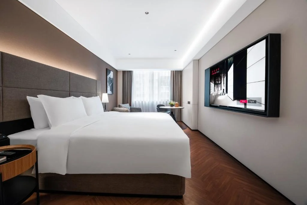 Spacious modern hotel room with king bed, wood floors and desk by curtained window in a quiet off-season travel retreat.