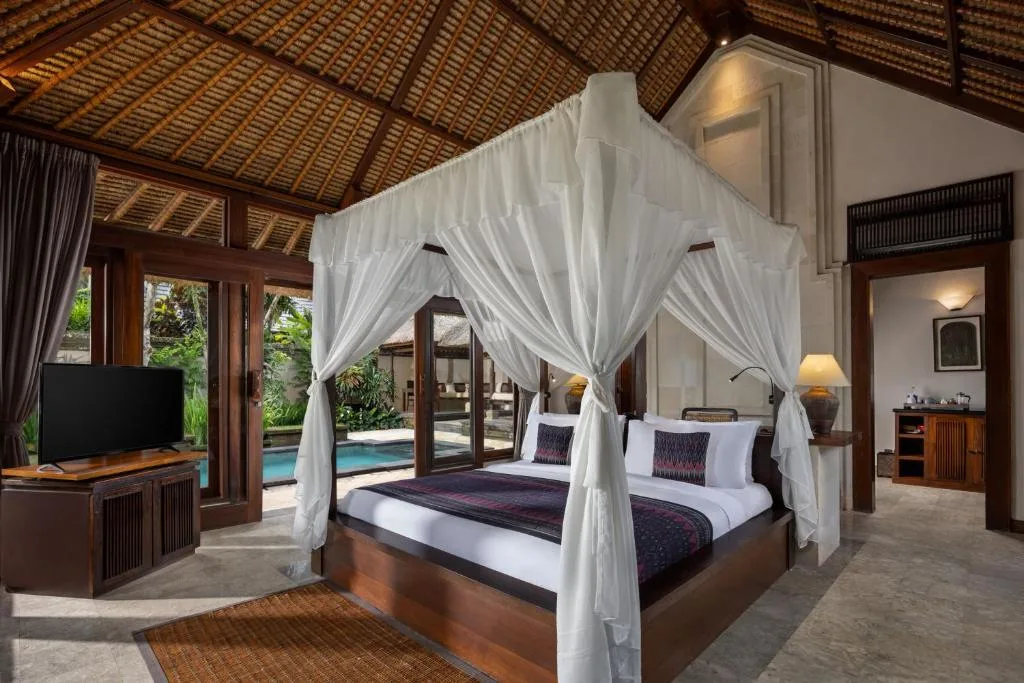 Serene off-season tropical villa bedroom with white canopy bed, private pool and lush garden seen through open wooden doors