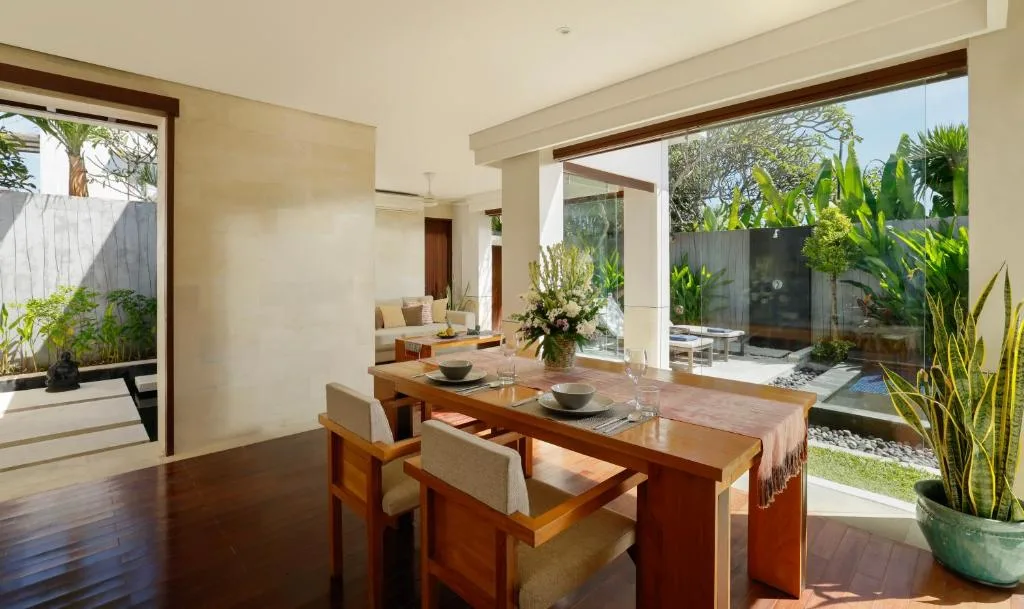 Quiet off-season villa: sunlit dining area overlooking lush tropical garden and private pool serenity.
